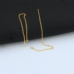 以下が含まれることがあります： 金色のチェーンのイヤリングのペア。片方のイヤリングはシンプルなチェーンで、もう片方はストレートの金色のバーがついたチェーンです。