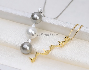 May include: A gold-tone necklace with a silver chain and three pearls. The pearls are gray, white, and gray. The necklace is on a white surface.