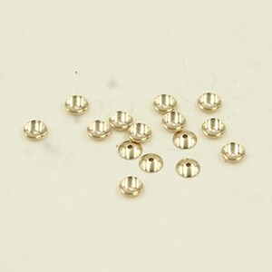 May include: A group of 15 gold-colored metal bead caps. The caps are round and have a slightly raised center.