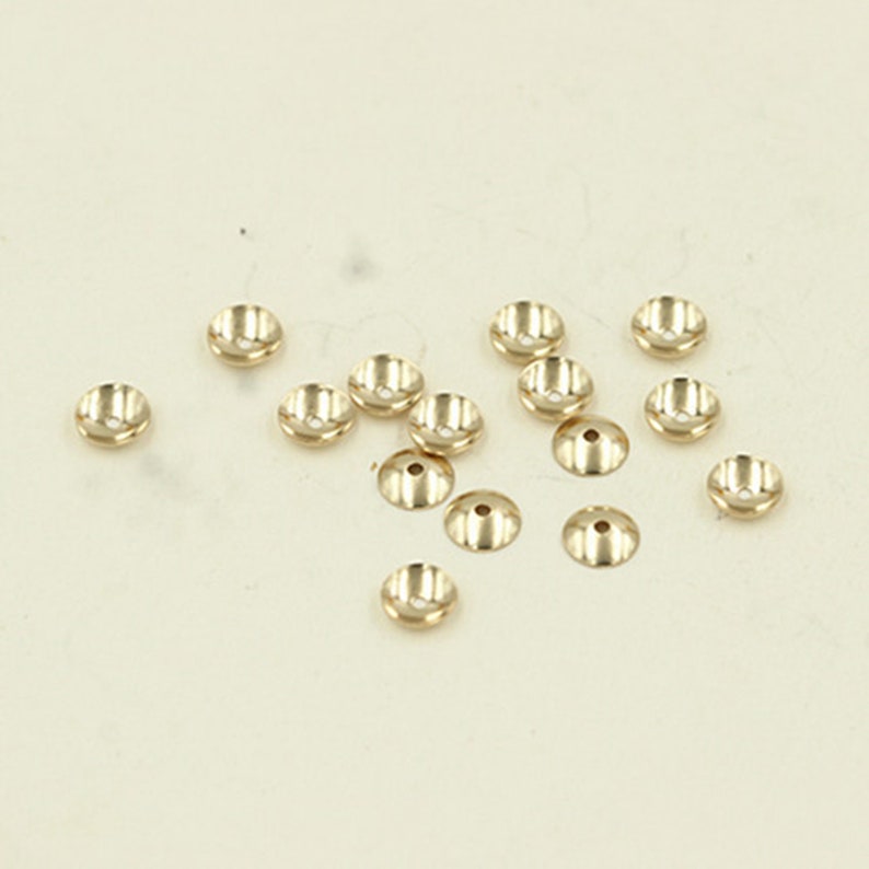 May include: A group of 15 gold-colored metal bead caps. The caps are round and have a slightly raised center.