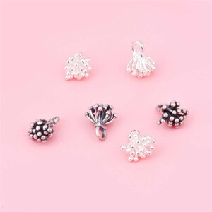 May include: Six silver and black metal bead caps with a flower-like design. The bead caps are small and delicate, with a loop at the top for attaching to a necklace or bracelet.