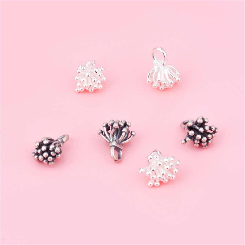 May include: Six silver and black metal bead caps with a flower-like design. The bead caps are small and delicate, with a loop at the top for attaching to a necklace or bracelet.
