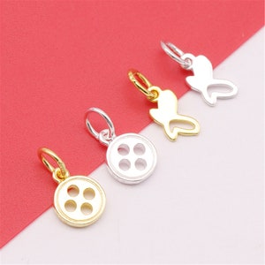 May include: Four gold and silver charms in the shape of buttons and butterflies. The charms are on a red and white background.