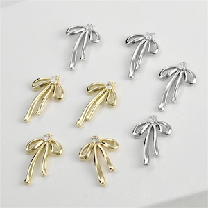 May include: Six silver and gold bow charms with clear rhinestones. The charms are perfect for jewelry making or adding a touch of sparkle to crafts.