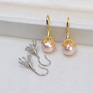 May include: Elegant gold-tone drop earrings featuring a light pink pearl. The earrings have a unique design with a gold-tone floral-like cage holding the pearl. The earrings are displayed on a white surface.