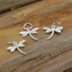 May include: Three silver dragonfly charms with a loop for attaching to jewelry. The dragonflies are detailed and have a textured finish.