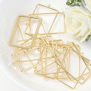 May include: A collection of gold-colored metal geometric frame pendants. The pendants are in square and diamond shapes, with a small loop at the top for attaching to a chain or other jewelry component. The frames are empty inside.