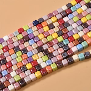 May include: A strand of colourful ceramic square beads. The beads are in various shades of blue, green, yellow, orange, red, pink, purple, and brown. The beads are arranged in a staggered pattern.