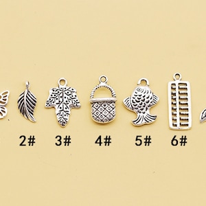 May include: Seven silver charm pendants with different designs: butterfly, leaf, tree, basket, fish, abacus, and mermaid tail. The charms are numbered 1 through 7.
