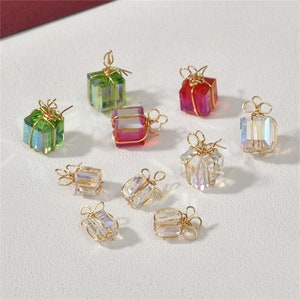 May include: Assortment of nine gold wire wrapped gift box charms with iridescent glass accents. The charms are in various colours, including green, red, and clear.