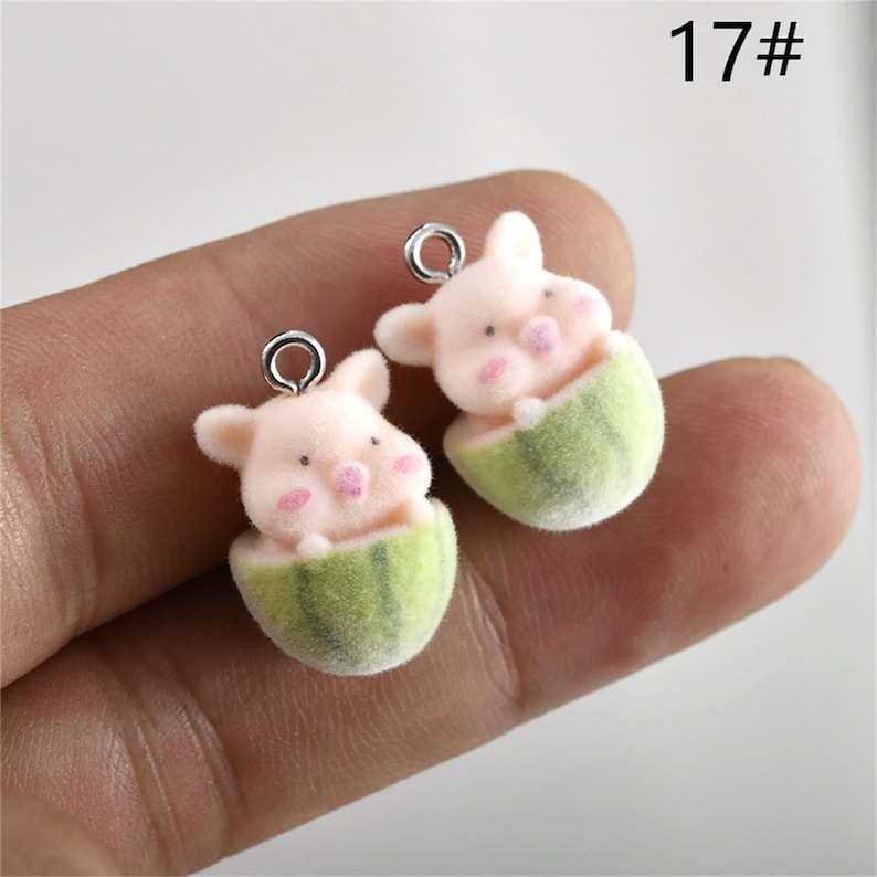 May include: Two pink pig charms with watermelon accents. The charms are made of felt and have silver jump rings. The charms are approximately 2 inches tall.