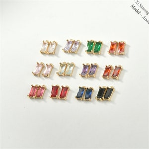 Peut inclure: Assortiment de breloques de boucles d'oreilles dorées avec des pierres de cristal de différentes couleurs. Les breloques sont de forme rectangulaire et ont deux petites boucles en haut.