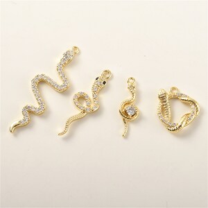 May include: Four gold-tone snake charm pendants with clear crystal accents. The charms are in different styles, including a coiled snake, a snake with its head raised, and a snake with its tail curled around its head.