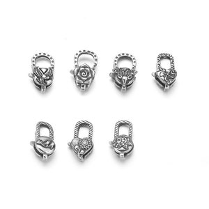 Könnte beinhalten: Acht silberfarbene Metallverschlüsse mit verschiedenen dekorativen Designs. Jeder Verschluss hat eine Schlaufe und einen Haken zum Anbringen an einer Kette oder einem Band.