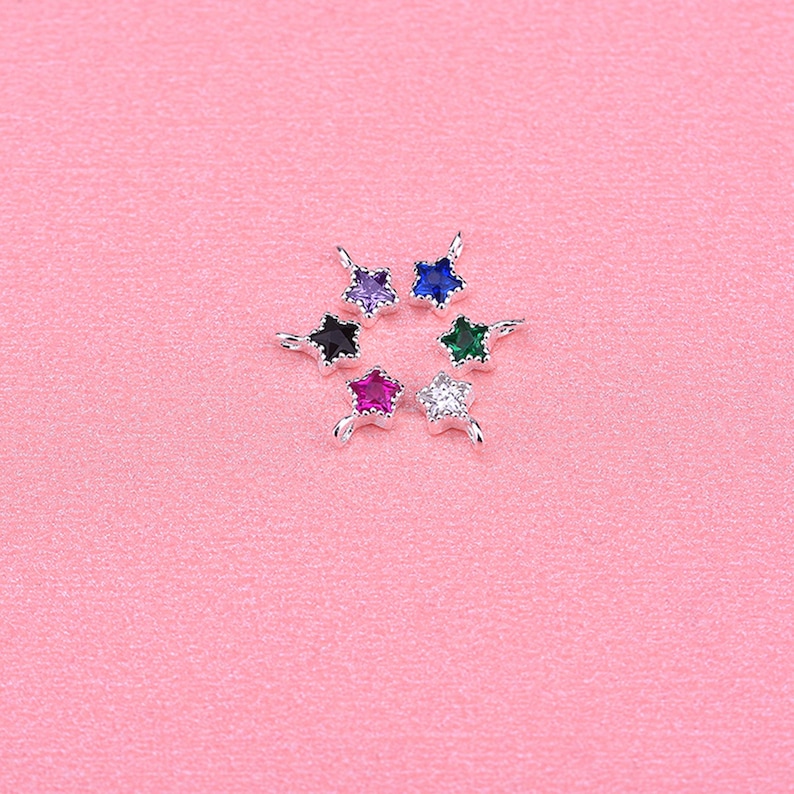 May include: Six silver star-shaped charms with different colored gemstones. The charms have a loop at the top for attaching to a necklace or bracelet. The gemstones are purple, blue, green, red, clear, and black.
