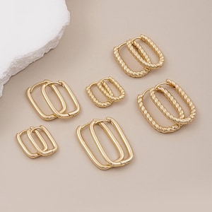 Könnte beinhalten: Eine Auswahl an goldfarbenen Creolen in verschiedenen Größen und Designs. Die Ohrringe haben rechteckige und ovale Formen, einige mit einer gedrehten Seiltextur. Der Schmuck wird vor einem neutralen Hintergrund präsentiert.