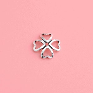 May include: Silver-toned metal charm shaped like a four-leaf clover with a hole in the center.