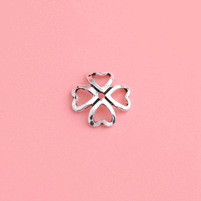 May include: Silver-toned metal charm shaped like a four-leaf clover with a hole in the center.