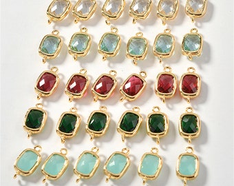May include: Twenty-four gold-toned metal charms with faceted glass inserts. The charms are in various colours, including clear, light blue, green, red, and dark green. Each charm has two loops for attaching to jewellery or other crafts. The charms are arranged in four rows of six. The text "size: 14*7mm" is printed below the charms.