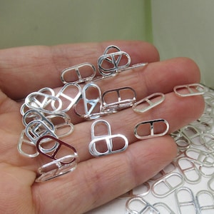 Könnte beinhalten: Nahaufnahme einer Hand, die einen Stapel ovaler, silberfarbener Metall-Sprünge hält. Die Sprungringe haben an jeder Seite eine kleine Öffnung.