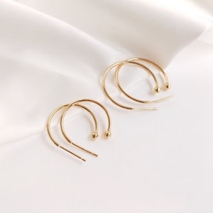 Pode incluir: Um par de brincos de argola de ouro com uma pequena bola no final de cada argola.