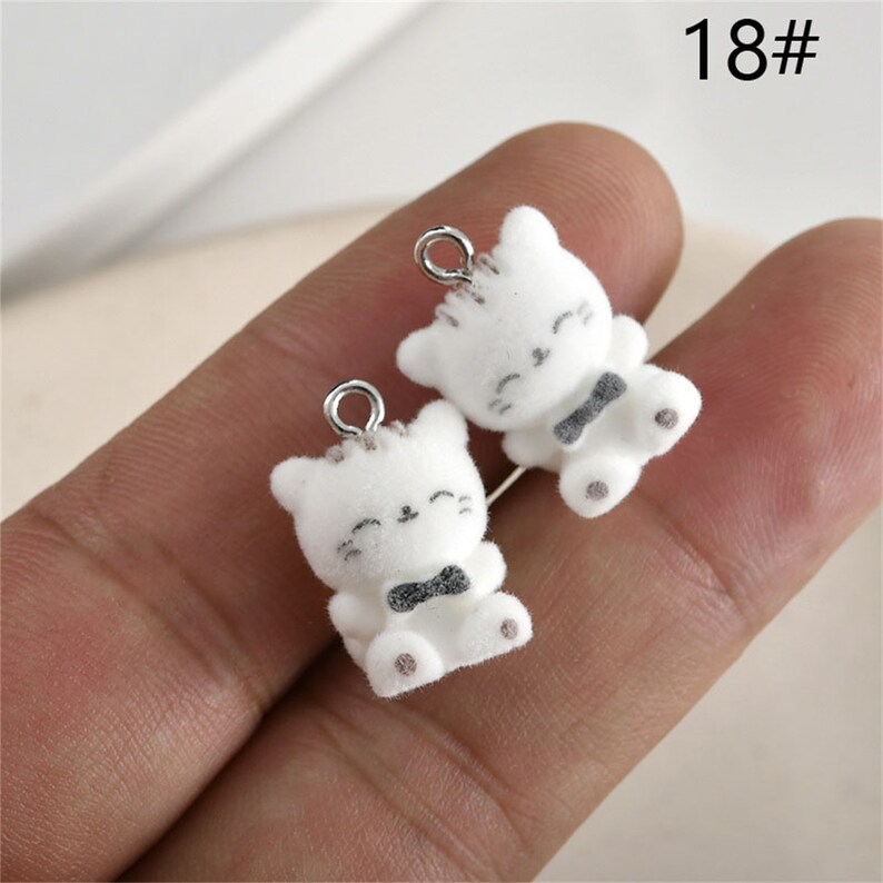May include: Two white cat charms with black bow ties and silver jump rings. The charms are about 2 inches tall.