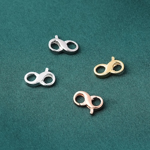 Puede incluir: Cuatro cierres de mosquetón metálicos en plata, oro y oro rosa. Los cierres tienen forma de ocho, con una palanca con resorte para abrir y cerrar fácilmente. Los cierres se muestran sobre un fondo verde oscuro.