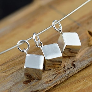 May include: Three silver cube charms hanging from a silver chain. The charms are smooth and shiny.