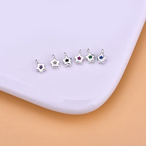 May include: Six silver star-shaped charms with different colored gemstones in the center. The colors are purple, black, red, green, green, and blue.
