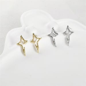 May include: A pair of star-shaped earrings with clear cubic zirconia stones. The earrings are available in gold and silver.