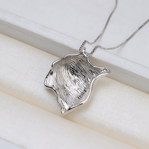 May include: A silver necklace featuring a distinctive, abstract pendant. The pendant is shaped like a wave or a leaf and has a textured surface.