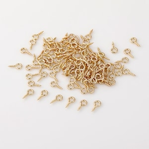 May include: A large pile of gold-coloured screw-in eyelet hooks. The hooks have a small loop at the top and a screw-like shaft.