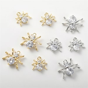 Pode incluir: Oito pingentes de aranha prateados e dourados com detalhes de strass transparente. Os pingentes são perfeitos para fazer joias ou para adicionar um toque assustador aos trabalhos manuais.