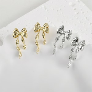 May include: Two pairs of earrings with a bow design. One pair is gold and the other is silver.
