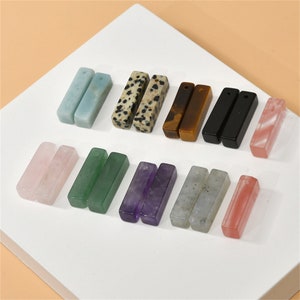 May include: A set of 10 pairs of gemstone bar earrings. The earrings are made of various stones, including amethyst, rose quartz, green aventurine, dalmatian jasper, tiger's eye, black onyx, labradorite, and white agate.