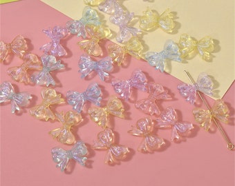 May include: A collection of iridescent rainbow-colored bow-shaped resin embellishments. There are 20 bows in total, and they are scattered on a pink surface. The text "8#" is written in black on a yellow surface in the background.