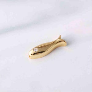 May include: A gold-coloured fish charm with a clear rhinestone in the centre. The charm is a popular choice for jewellery making and crafting.