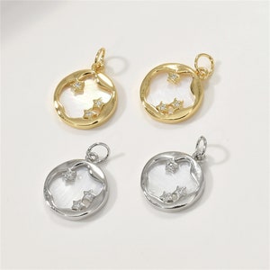 Puede incluir: Cuatro colgantes redondos con una incrustación de concha blanca y tres pequeños diamantes de imitación en forma de estrella. Dos colgantes son de color dorado y dos son de color plateado.