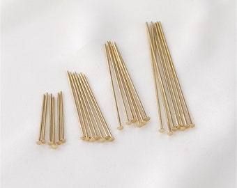 May include: A collection of gold-colored head pins in varying lengths, arranged on a white surface. The pins have a flat, circular head and a slender, straight shaft. The image showcases several bundles of these pins, ideal for jewelry making or crafting.