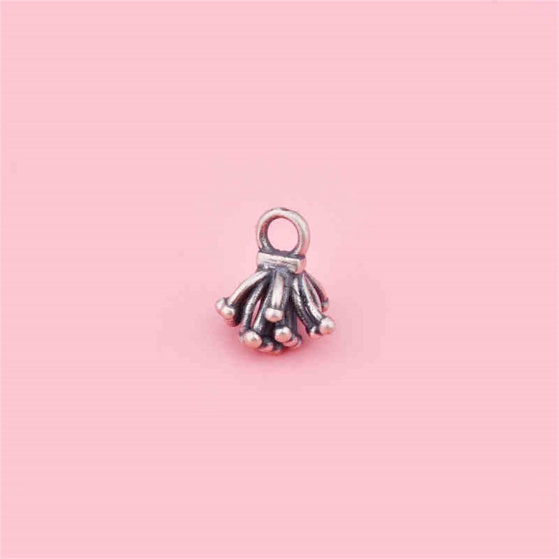 May include: Silver charm with a delicate, intricate design resembling a cluster of small flowers or a firework burst.