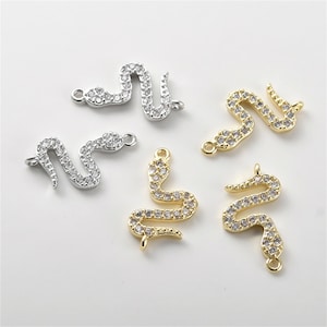 Op de afbeelding: Vijf gouden en zilveren slangencharms met heldere kristallen accenten. De charms hebben een lus aan de bovenkant om aan sieraden te bevestigen.