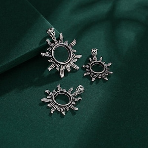 Pode incluir: Três pingentes de sol de prata com um design de filigrana. Os pingentes estão sobre um fundo verde.