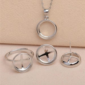 May include: A collection of silver-toned jewelry components, including a pendant, ring, earrings, and a pair of earring settings. Each piece features a circular frame with a cross-shaped design in the center, perfect for jewelry making.