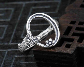 May include: A silver ring with a circular design and floral accents. The ring is open in the center, allowing for a stone or other embellishment to be inserted.