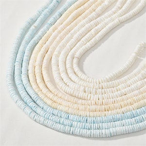 May include: A strand of white and light blue shell beads. The beads are small and round, and they are strung together on a thin cord. The beads are arranged in a gradient, with the white beads at the top and the light blue beads at the bottom.