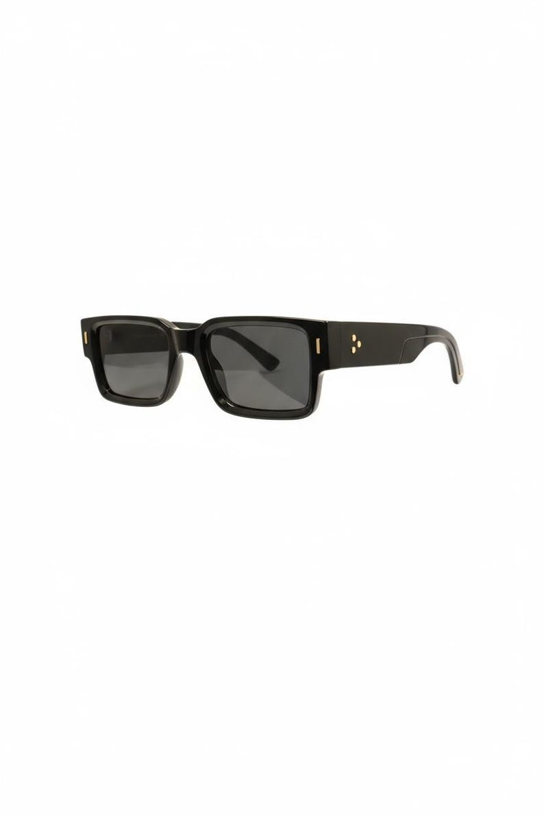 K&ouml;nnte beinhalten: Schwarze Sonnenbrille mit rechteckigem Rahmen und dunklen Gl&auml;sern. Die Sonnenbrille hat goldfarbene Akzente an den B&uuml;geln und am Rahmen. Das Gesamtdesign ist elegant und modern, passend f&uuml;r verschiedene Stile.