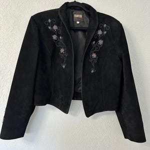 May include: Black suede jacket with floral embroidery in silver, pink, and clear beads. The jacket has a notched collar and long sleeves. The brand name "Frontier" is visible on a tag inside the collar.