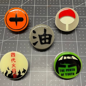 May include: Five round, colorful, decorative, adhesive phone grips with different designs. The designs include a black cross on an orange background, a black and white swirl on a gray background, a black and white stylized face on a green background, a black and white flame design on a yellow background, and a red and white circle on a gray background.