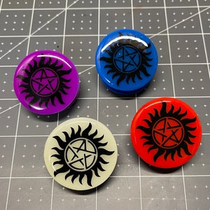 May include: Four round, colorful phone grips with a black pentagram inside a sunburst design. The grips are purple, blue, white, and red.