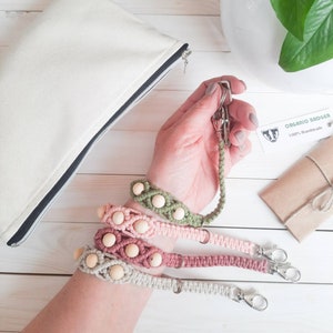 May include: Four handmade keychains with wooden beads and macrame cord in shades of green, pink, and beige. Each keychain has a silver metal clasp. The text "ORGANIC BADGER 100% Handmade" is visible on a small tag.